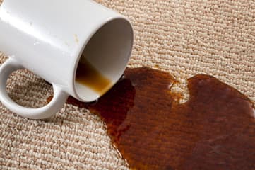 A tipped white mug spilling coffee onto beige carpet.